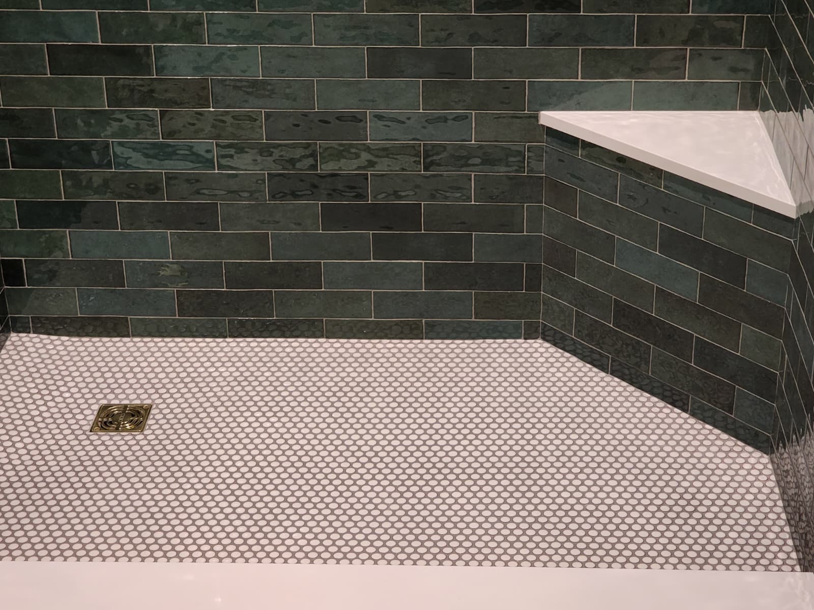 Finished walk-in shower with dark green subway tile, penny tile floor, recessed niche and corner bench
