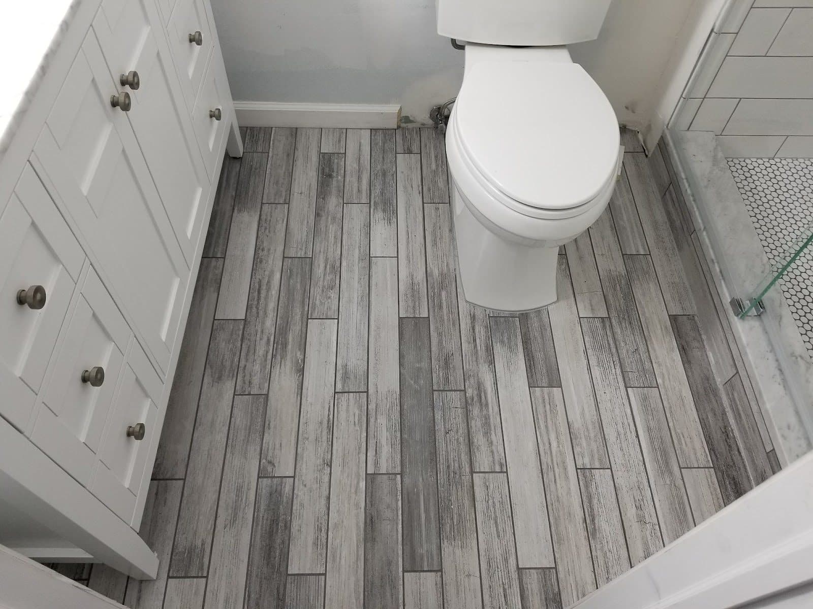 Bathroom floor in gray wood-look plank tile next to a vanity and toilet